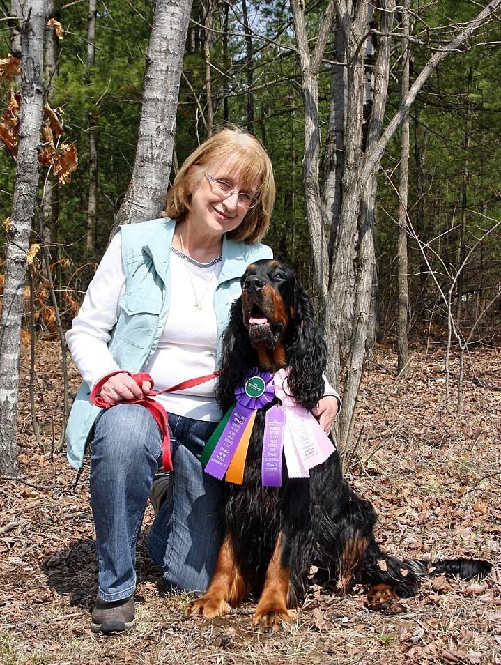 Susan with a brown and black curly haired spaniel with ribbons around the neck.